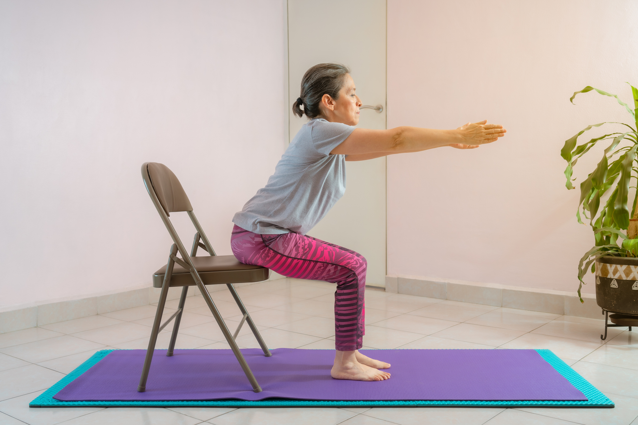 woman seated on a chair on a yoga mat stretching her arms out in from of her