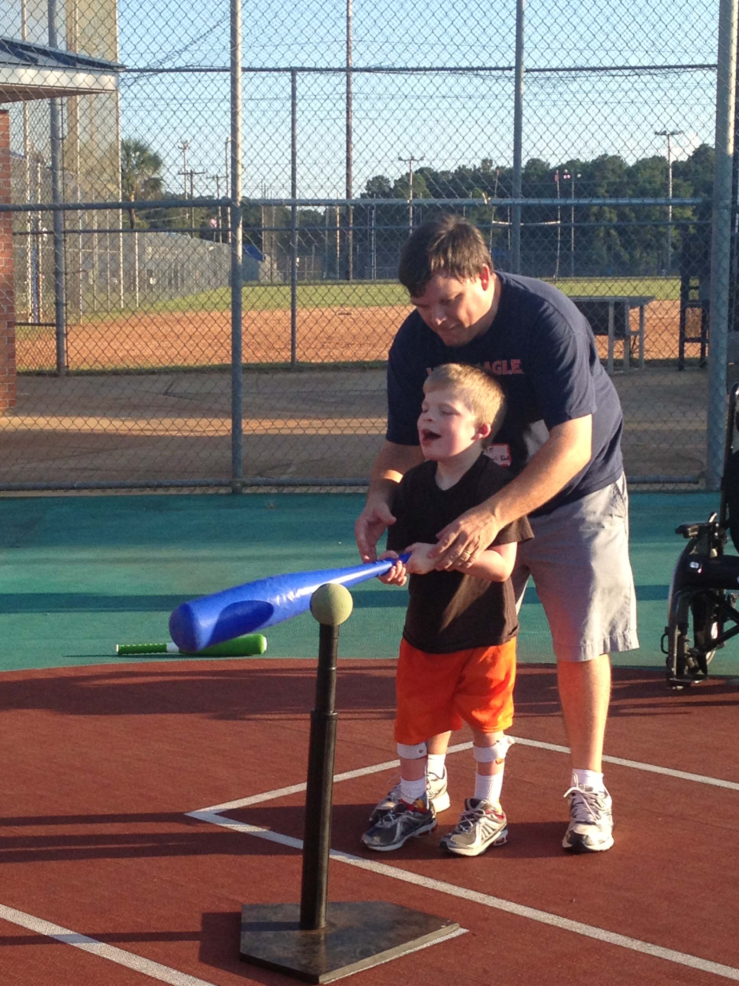 a child and volunteer hitting a ball off a tee at Miracle Sports