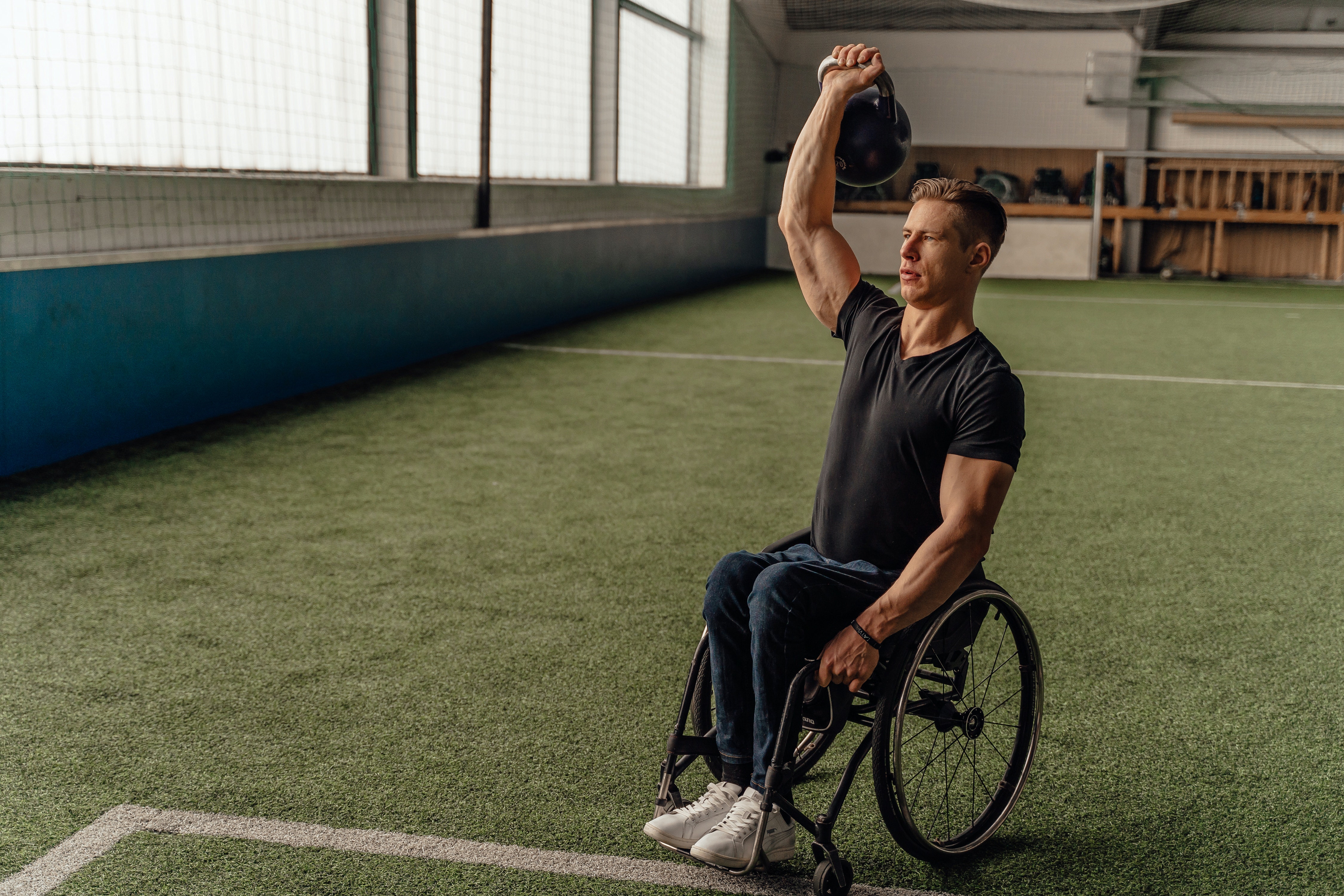 Man in a wheelchair lifting a kettlebell weight above his head